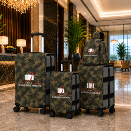 Trois enveloppes à bagages roulantes en motif camouflage vert sont exposées dans le hall d’un hôtel de luxe. L’ensemble comprend une grande valise, une valise moyenne et un sac à dos, tous portant le logo « THE LUGGAGE WRAPS ».