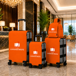 Trois housses à bagages orange recouvrant des valises à roulettes et un sac à dos orange assorti sont exposés dans le hall d'un hôtel de luxe. Les housses arborent le logo et l'inscription « THE LUGGAGE WRAPS » imprimées en blanc.