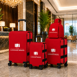 Trois enveloppes rouges sur des valises à roulettes et un sac à dos de voyage rouge assorti, exposés dans le hall d’un hôtel de luxe. Le logo imprimé blanc indique « THE LUGGAGE WRAPS ».